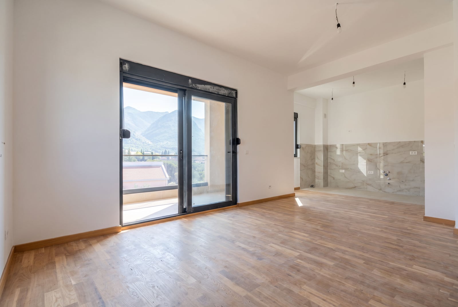 New living room with parquet flooring, panoramic window, and mountain view in an apartment in the city of Bar, Montenegro.
