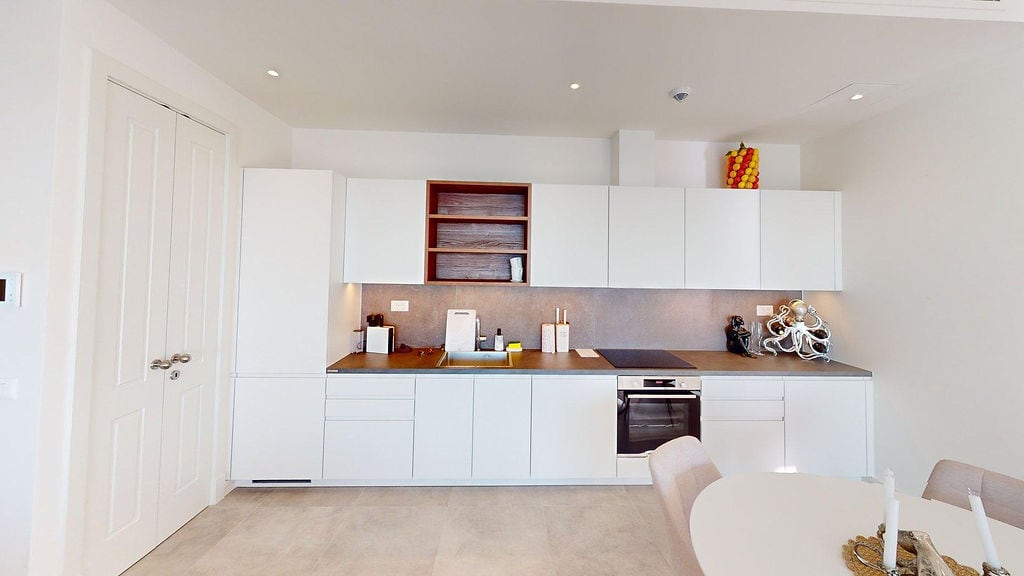 Modern white kitchen in a Lustica Bay apartment, Luštica, Montenegro: built-in appliances and dining area.