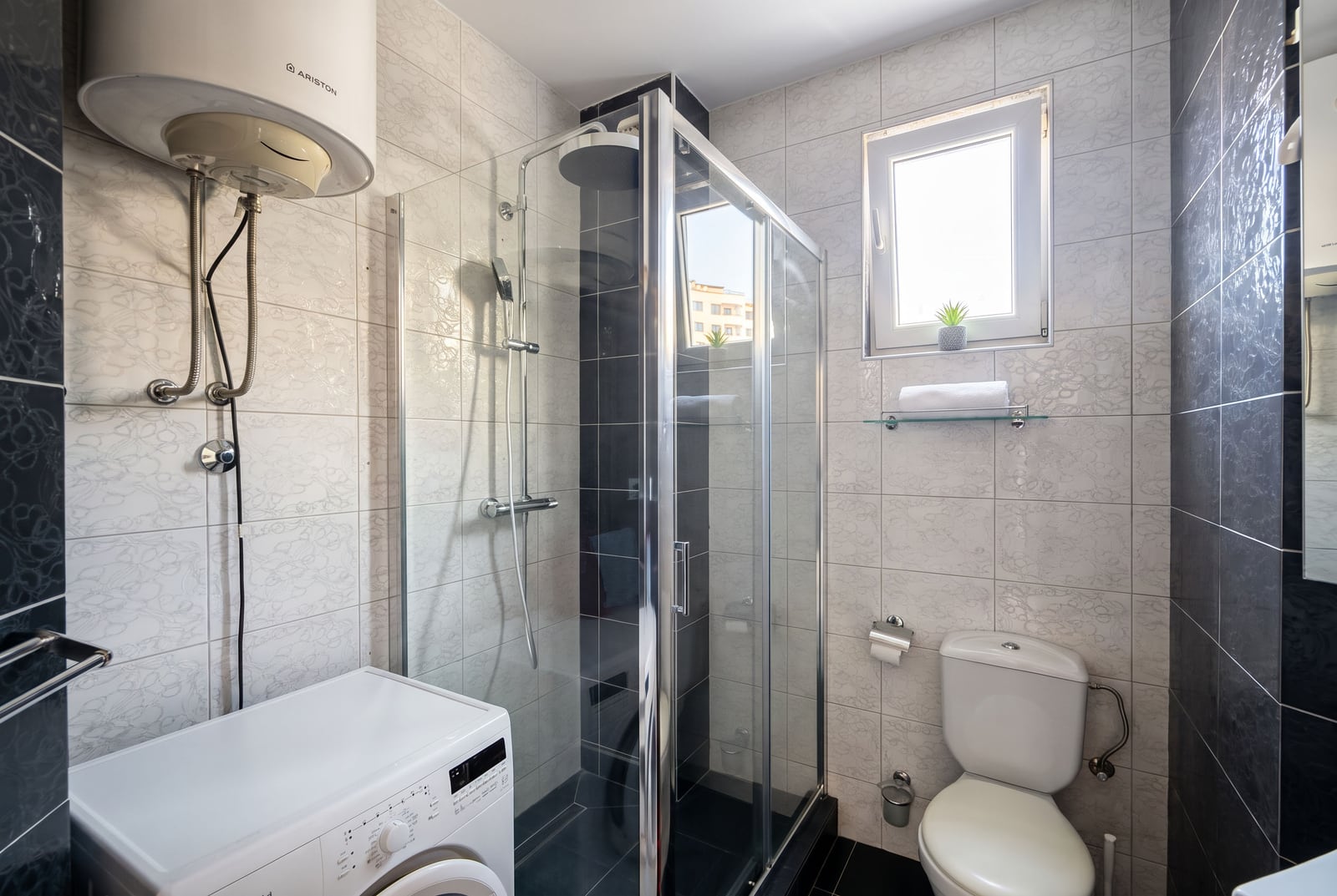 Modern bathroom with a shower cabin, washing machine, and water heater in an apartment in Bečići, Montenegro.