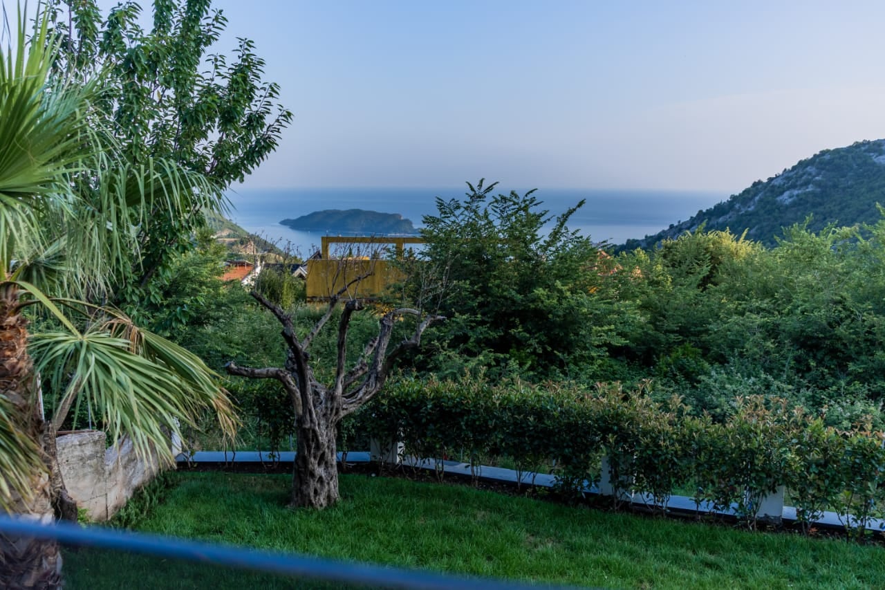 Sea view and island view from the villa terrace in Budva, Montenegro: green garden, palm trees, and panoramic landscape.