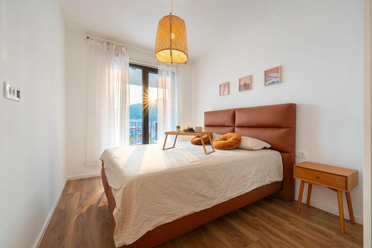 Bright bedroom featuring a double bed with a brown leather headboard, wooden nightstand, and wicker pendant light.