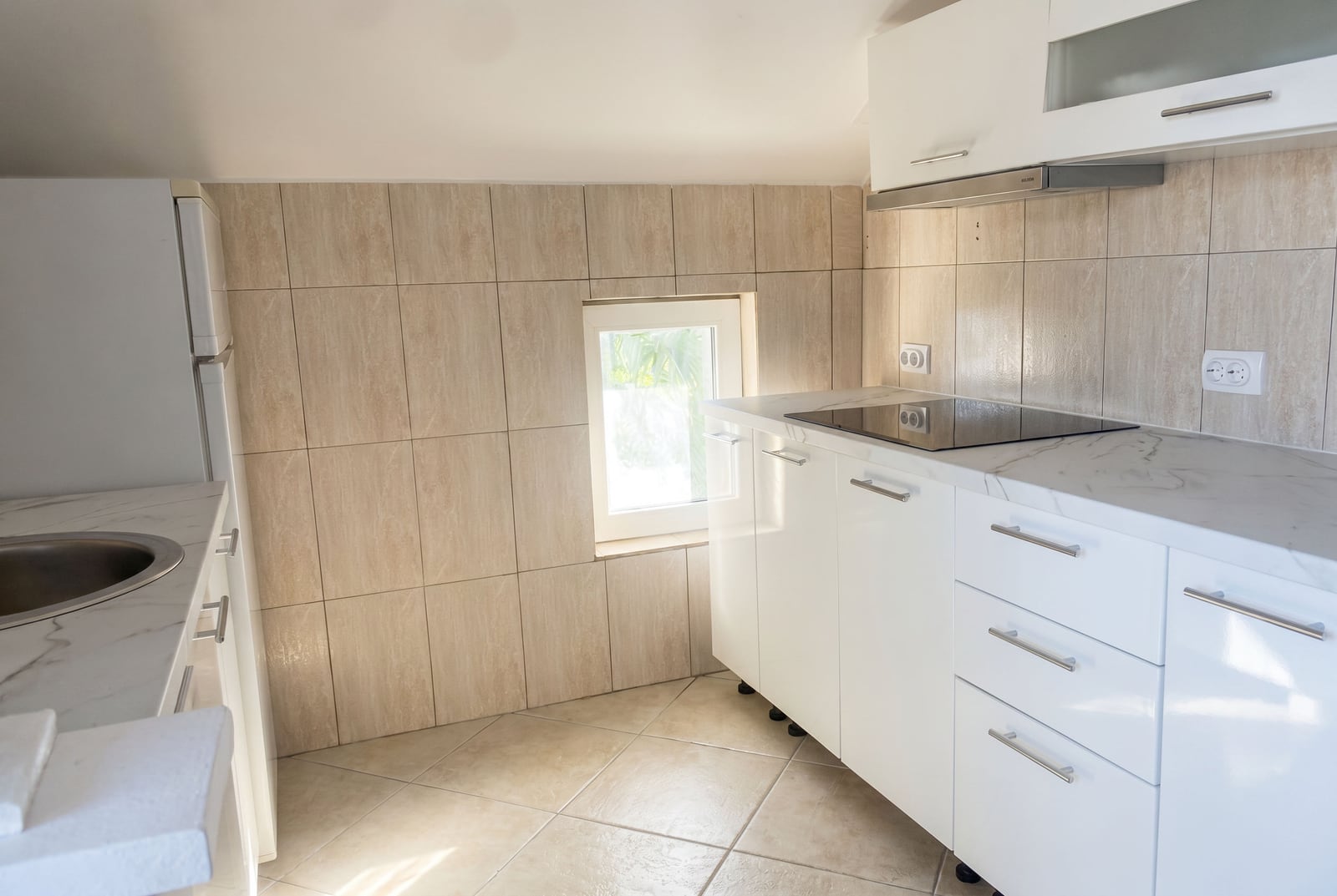 Modern white kitchen in a house in Krašići, Montenegro: light-colored tiles, built-in appliances, and a marble countertop.