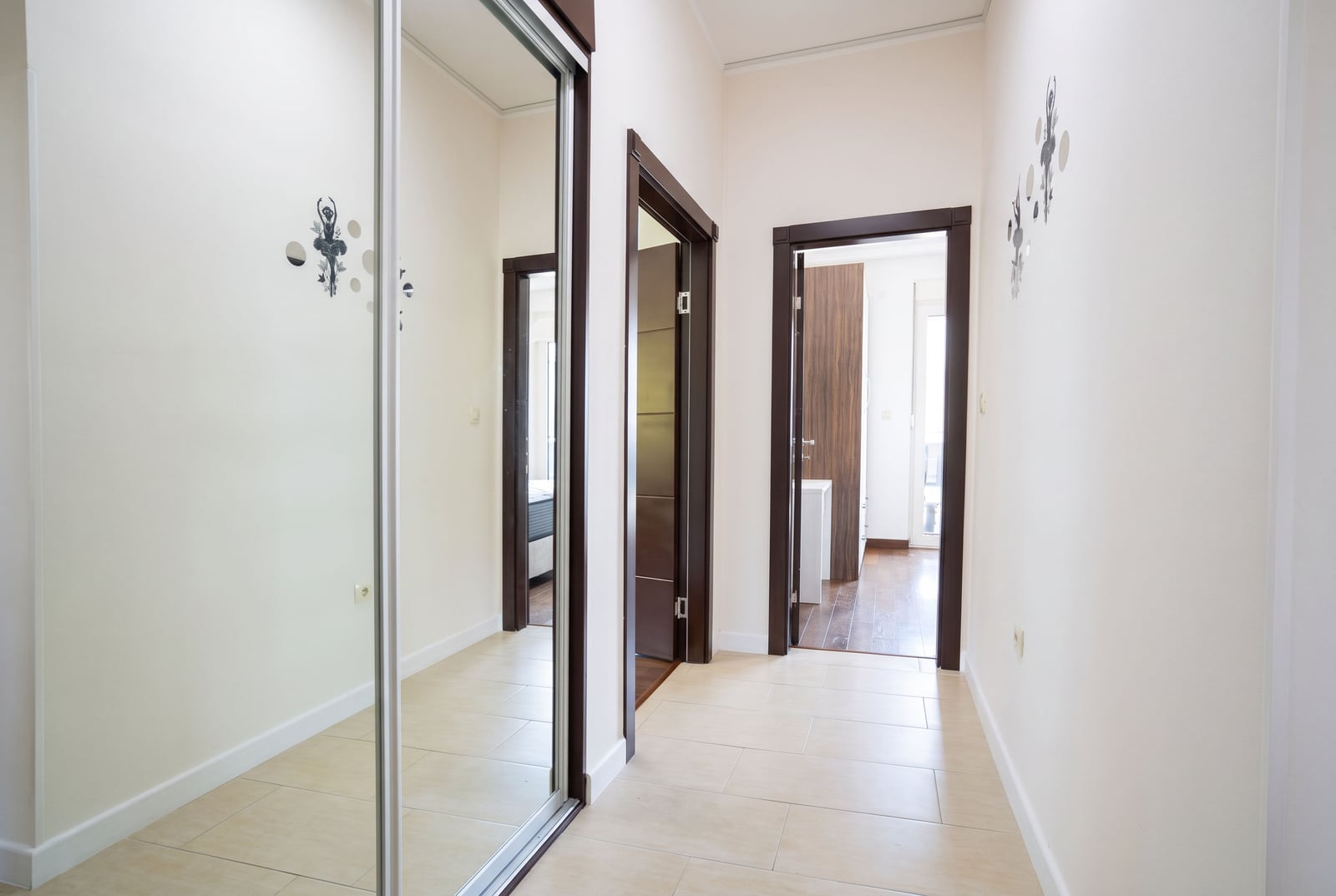 Hallway with a mirrored wardrobe door, light walls, decorative stickers, and multiple dark wood door frames leading to other rooms.