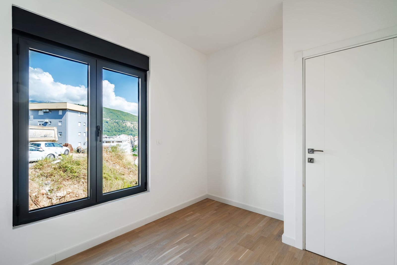 Bright bedroom with parquet flooring and mountain views in a residential complex, Budva, Montenegro. Modern finishes and white walls.