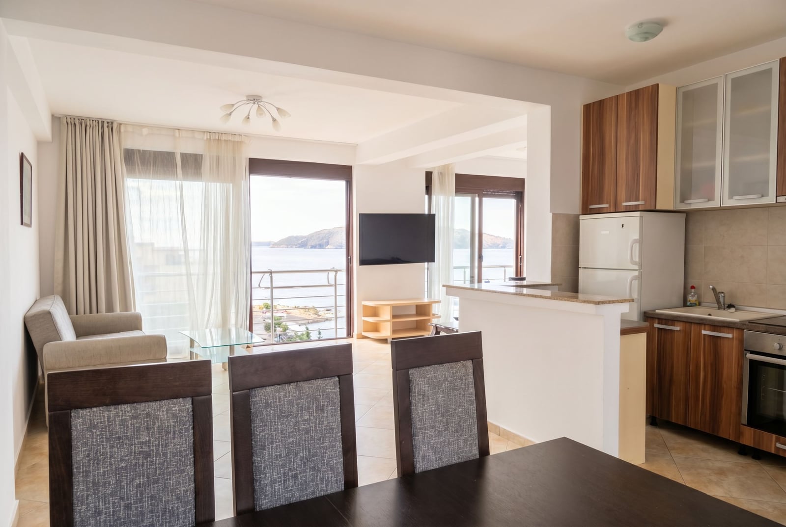 Living room with kitchen in an apartment in Rafailovici, Montenegro: sea view, modern furniture, and panoramic windows.