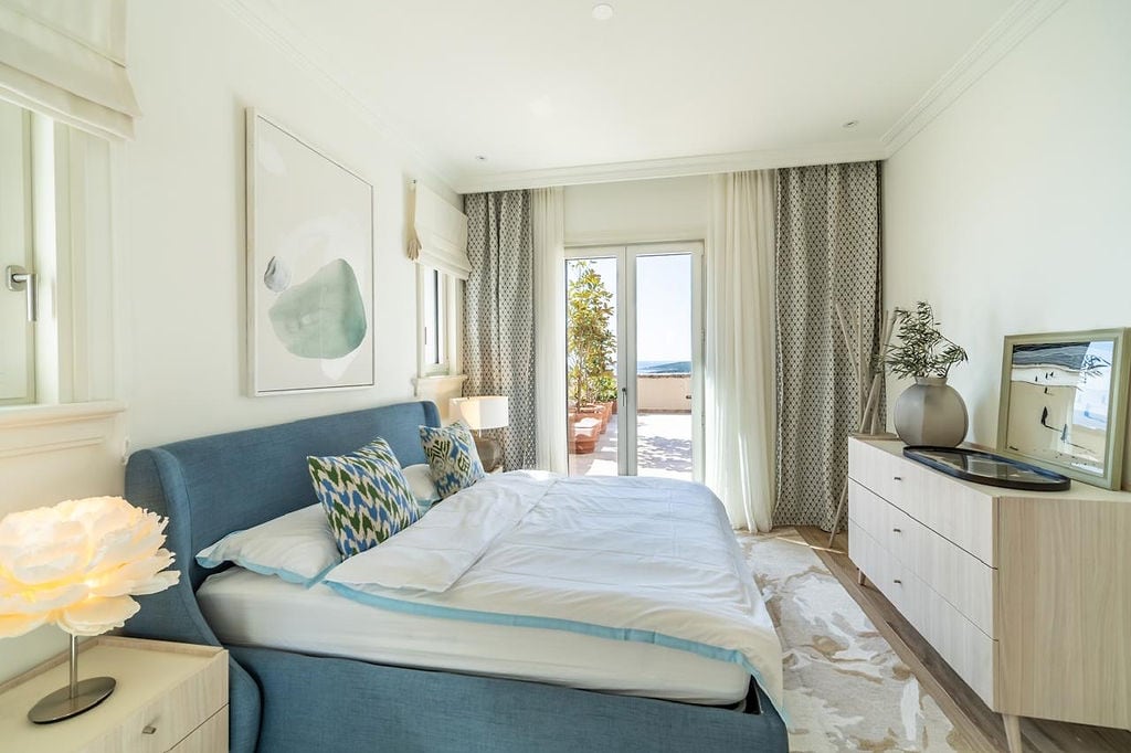 Bright bedroom in an apartment, Luštica, Montenegro: blue bed, dresser, and access to a terrace with a sea view.