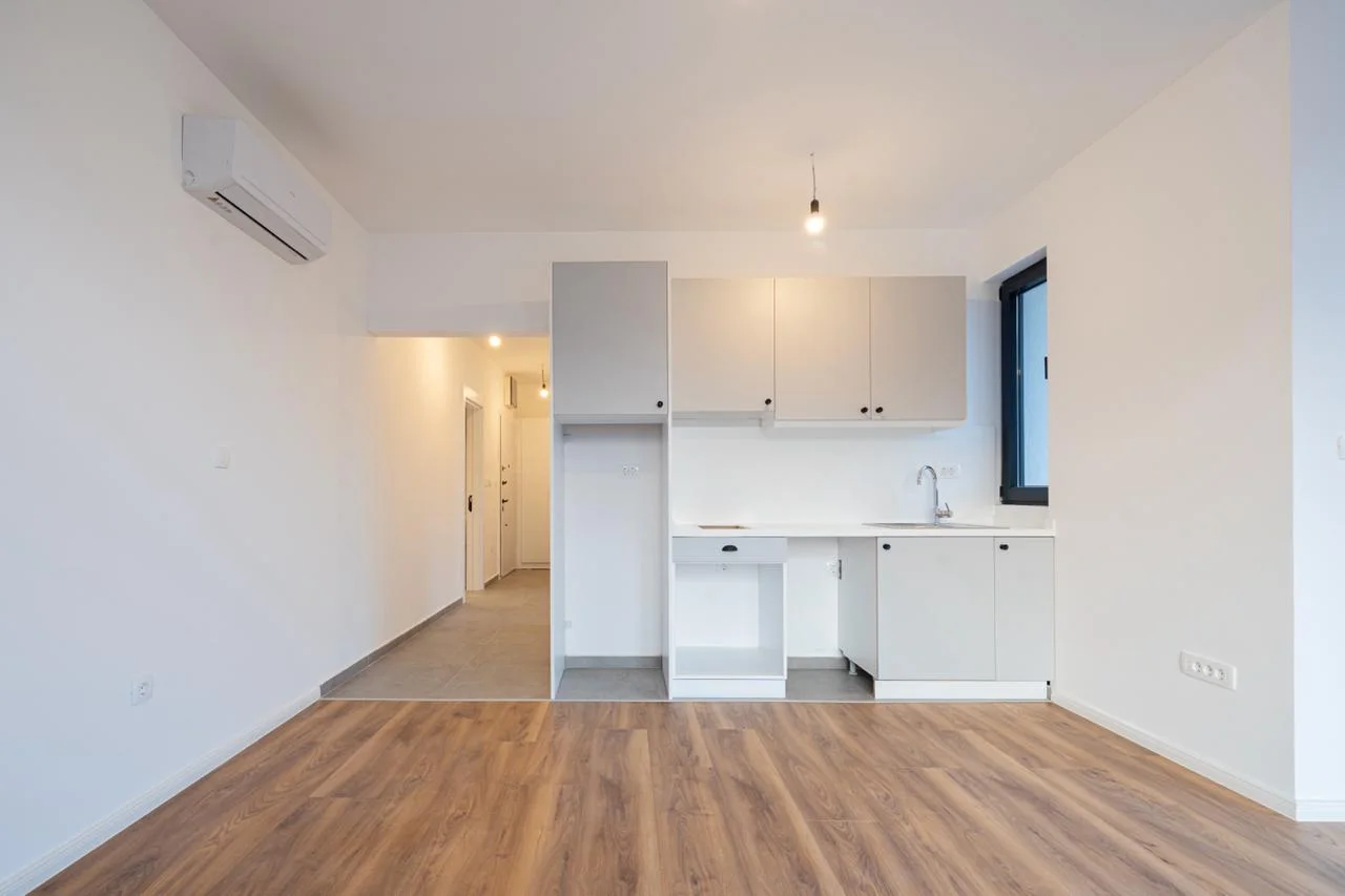 Small white kitchen with cabinets, sink, and wood flooring in an open-plan layout.