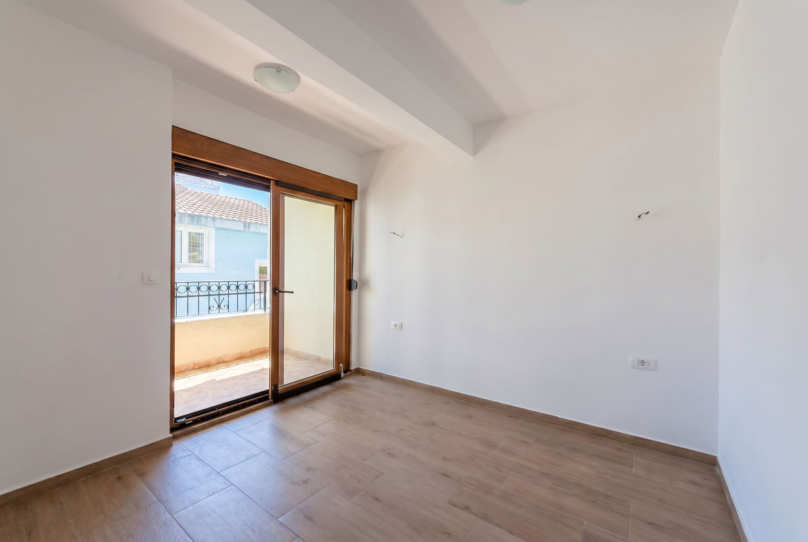 Bright bedroom with balcony access in an apartment, Budva, Montenegro: wood-look laminate flooring and panoramic door.