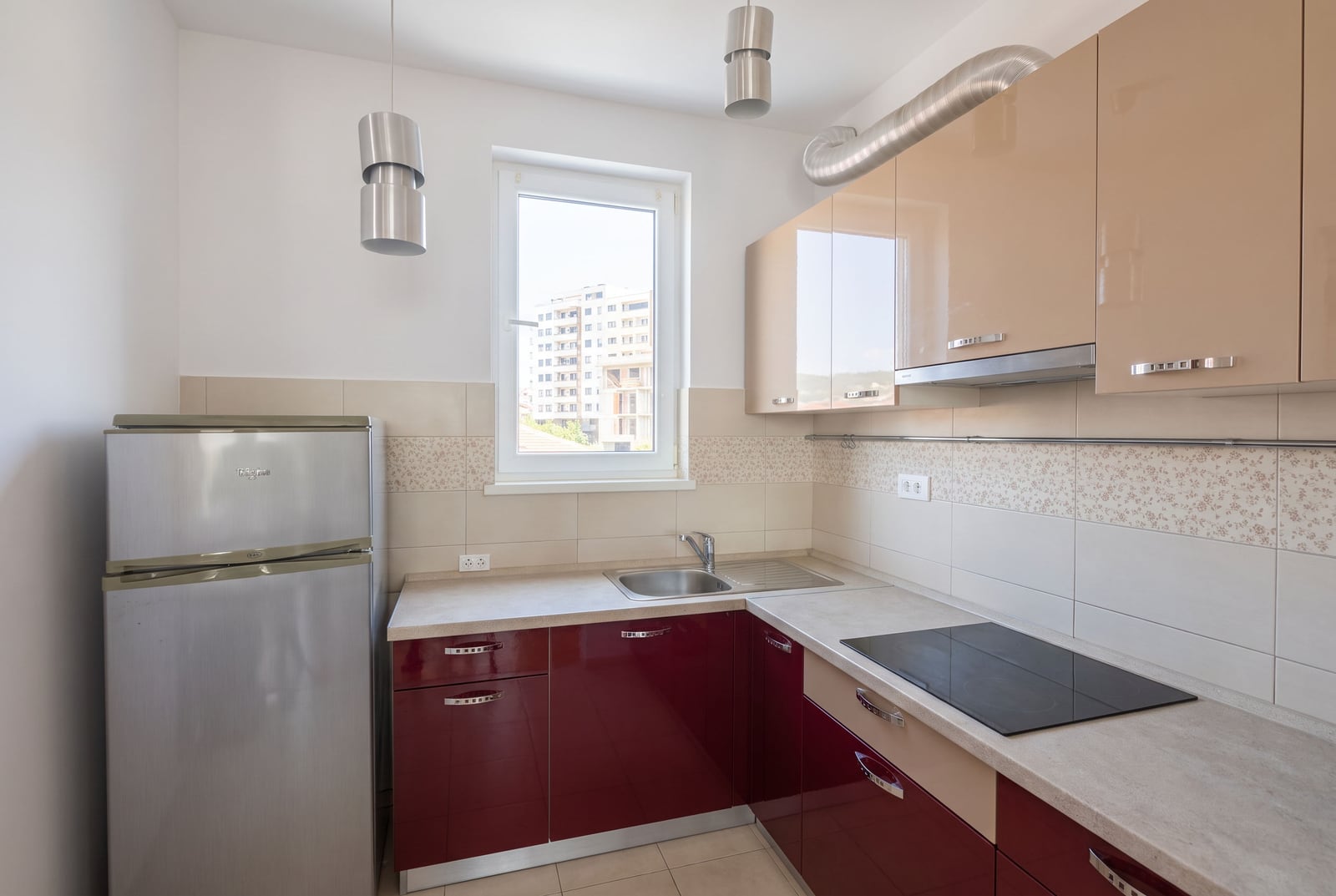 Modern kitchen with beige and burgundy facades, appliances, and a window in an apartment in Bečići, Montenegro