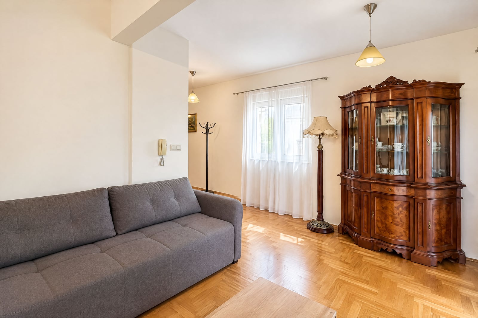 Living room featuring a grey sofa, antique wooden display cabinet, and parquet flooring.