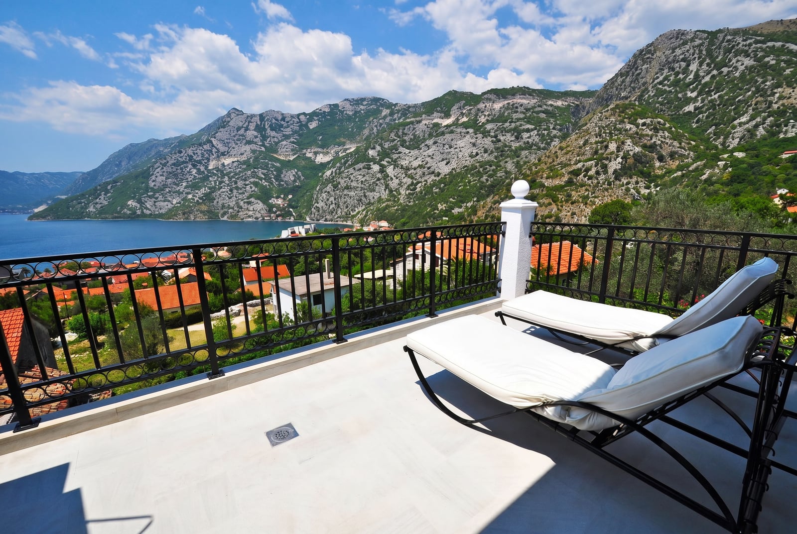 Penthouse terrace in Risan, Montenegro: view of the Bay of Kotor, mountains, and sun loungers on the balcony with wrought iron railing.