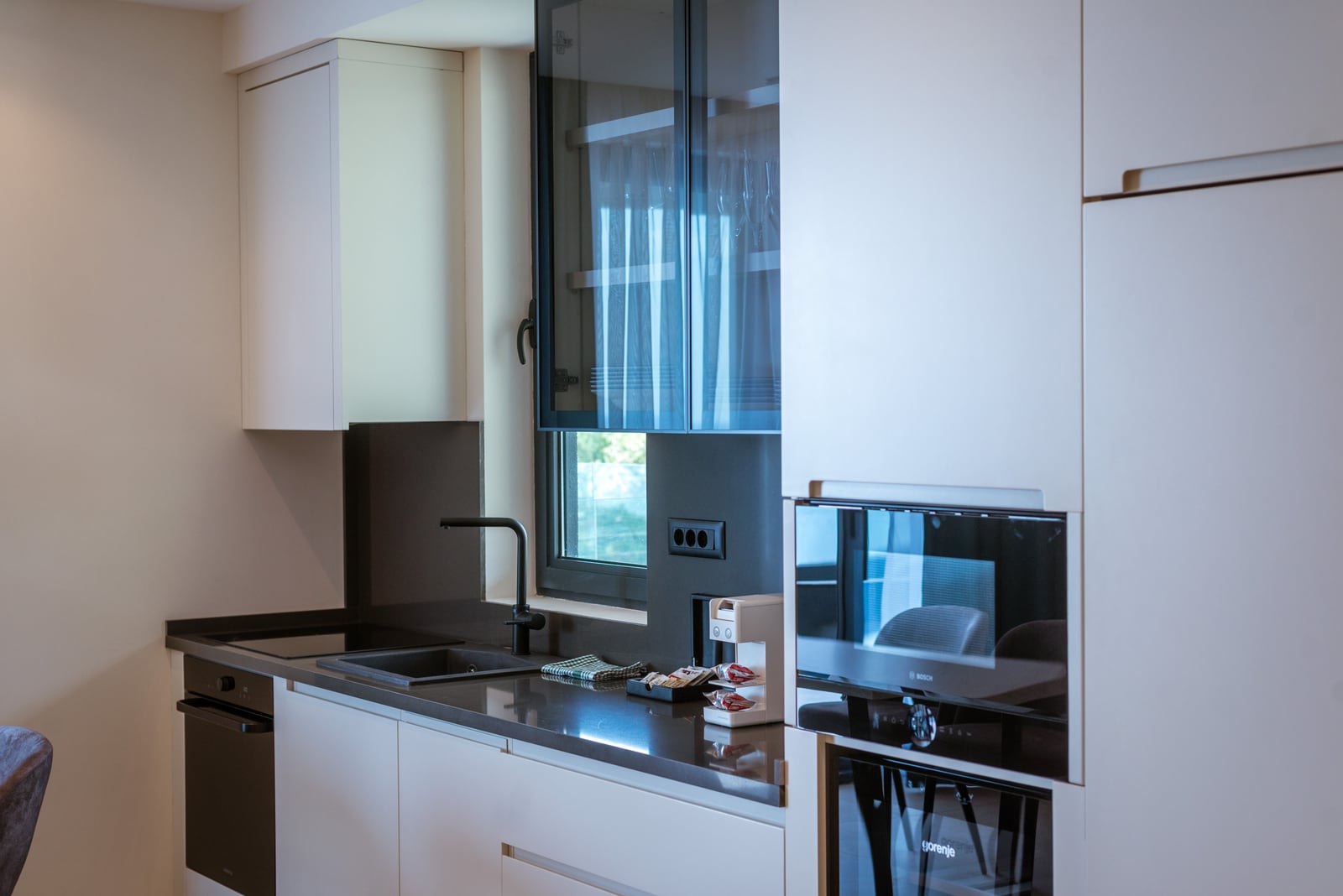Modern kitchen in an apartment in Bečići, Montenegro: white fronts, built-in Bosch and Gorenje appliances, dark countertop.