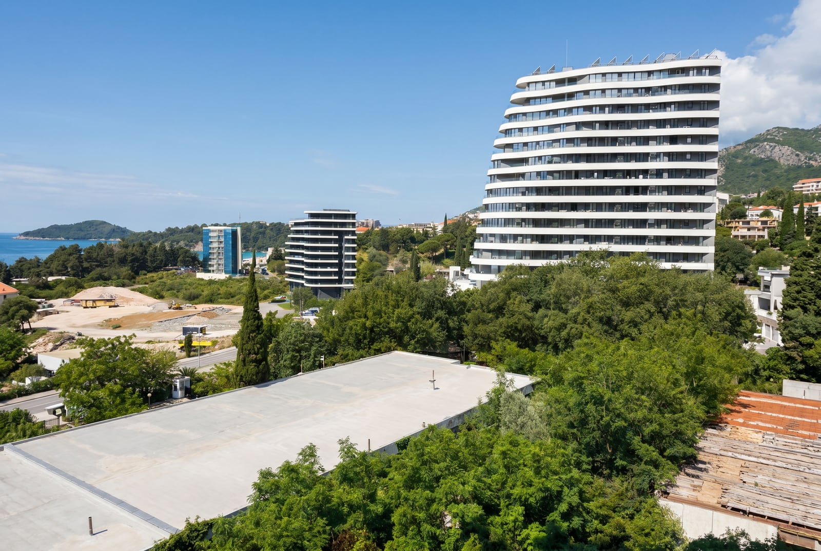 Modern residential complexes with panoramic terraces in Becici, Montenegro, featuring sea and mountain views surrounded by greenery.