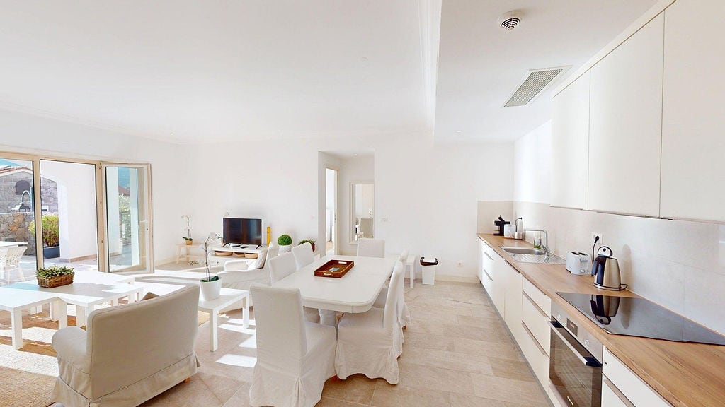 Bright living room with a modern-style kitchen in the Luštica apartments, Montenegro: white furniture and access to the terrace.