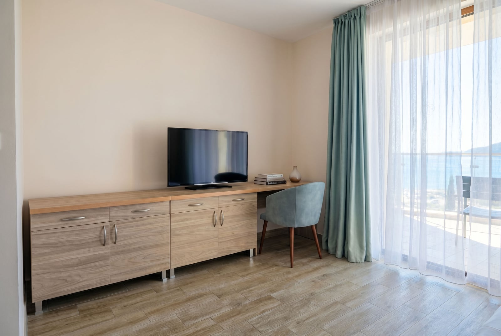 Living room with a TV area and access to a terrace with a sea view in an apartment, Bečići, Montenegro. Modern wood-finish furniture.