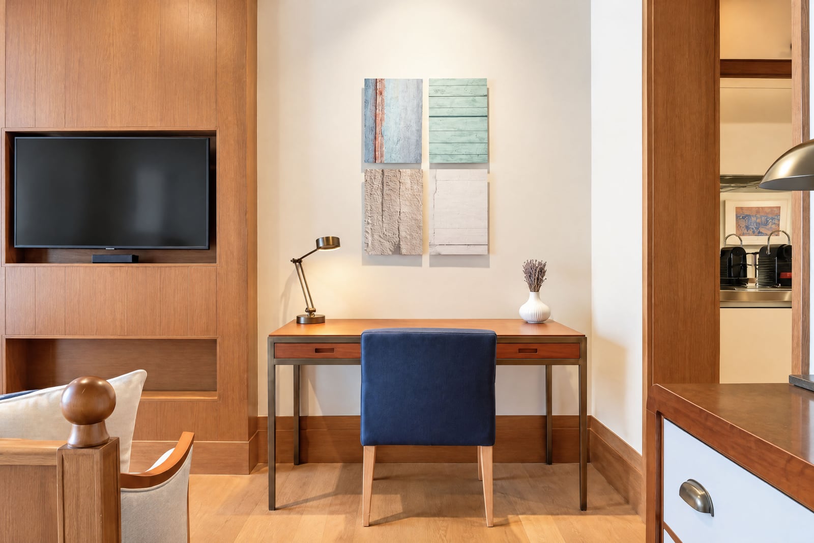 Wood desk with blue chair, built-in TV in wood paneling, and partial view of a bed headboard.