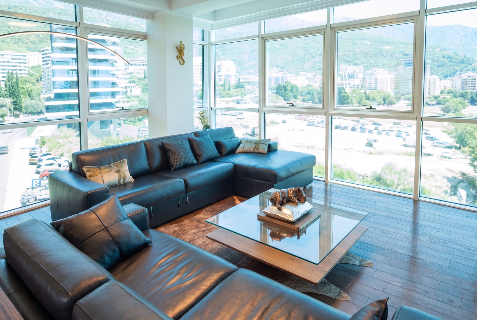 Modern living room with black leather sofa, glass coffee table, and panoramic windows overlooking city.