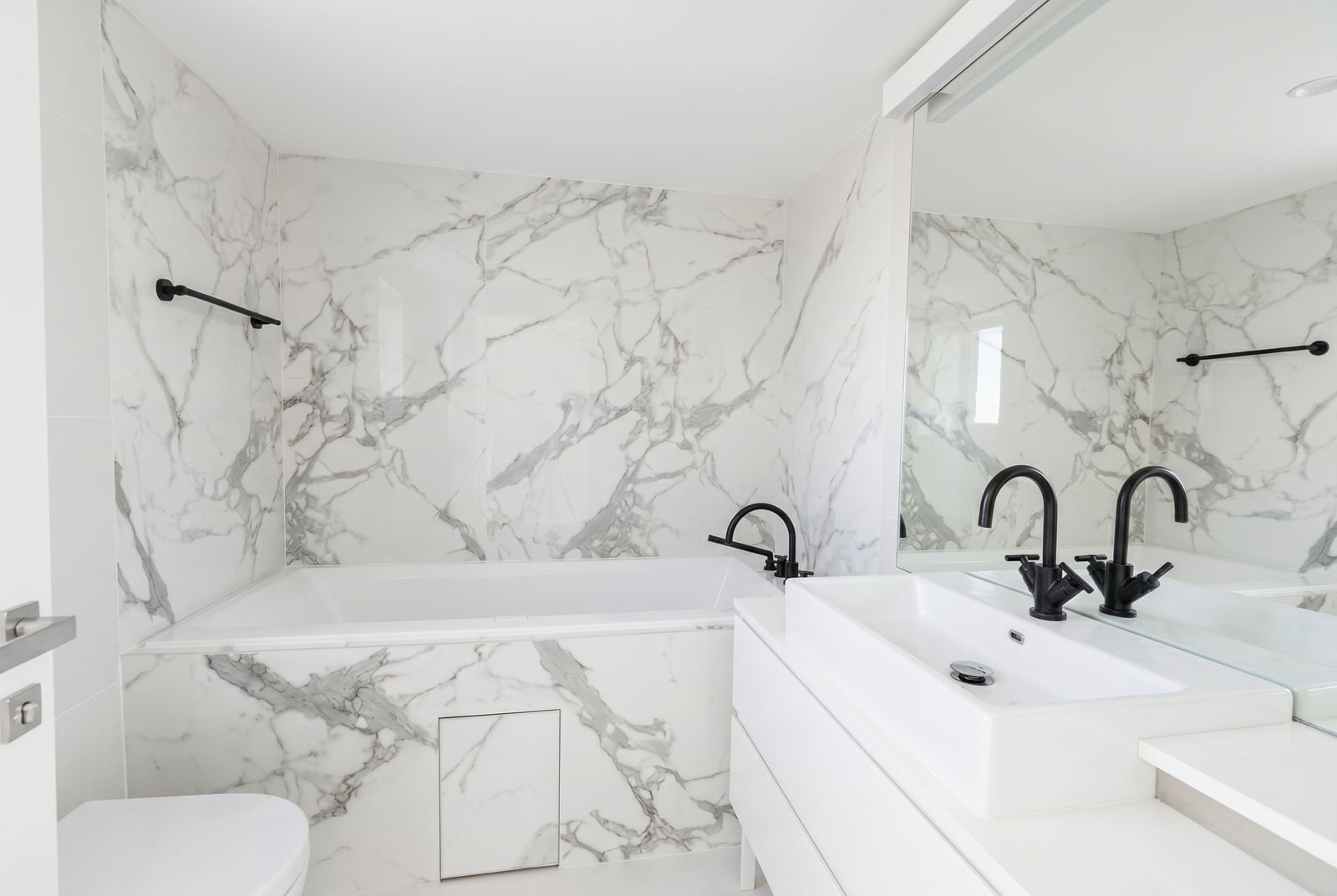 Modern bathroom in a Budva apartment, Montenegro: white marble-style finishes, black fixtures, and a mirror.