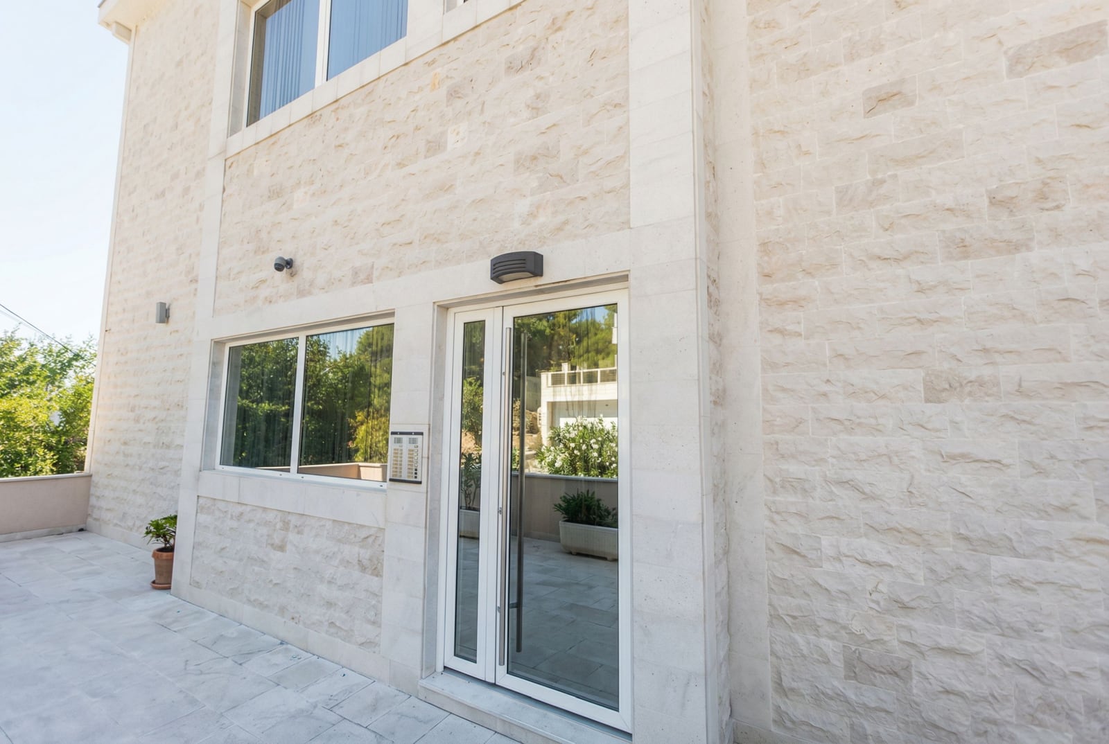 Facade of a modern house in Tivat, Montenegro: natural stone finish, glass entrance area, and terrace.