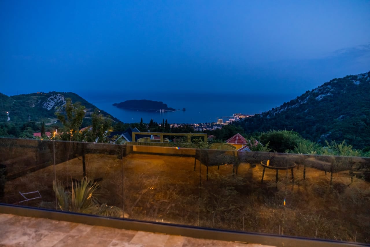 Panoramic view of the sea and St. Nicholas Island from the terrace of a villa in Budva, Montenegro, with glass railing.