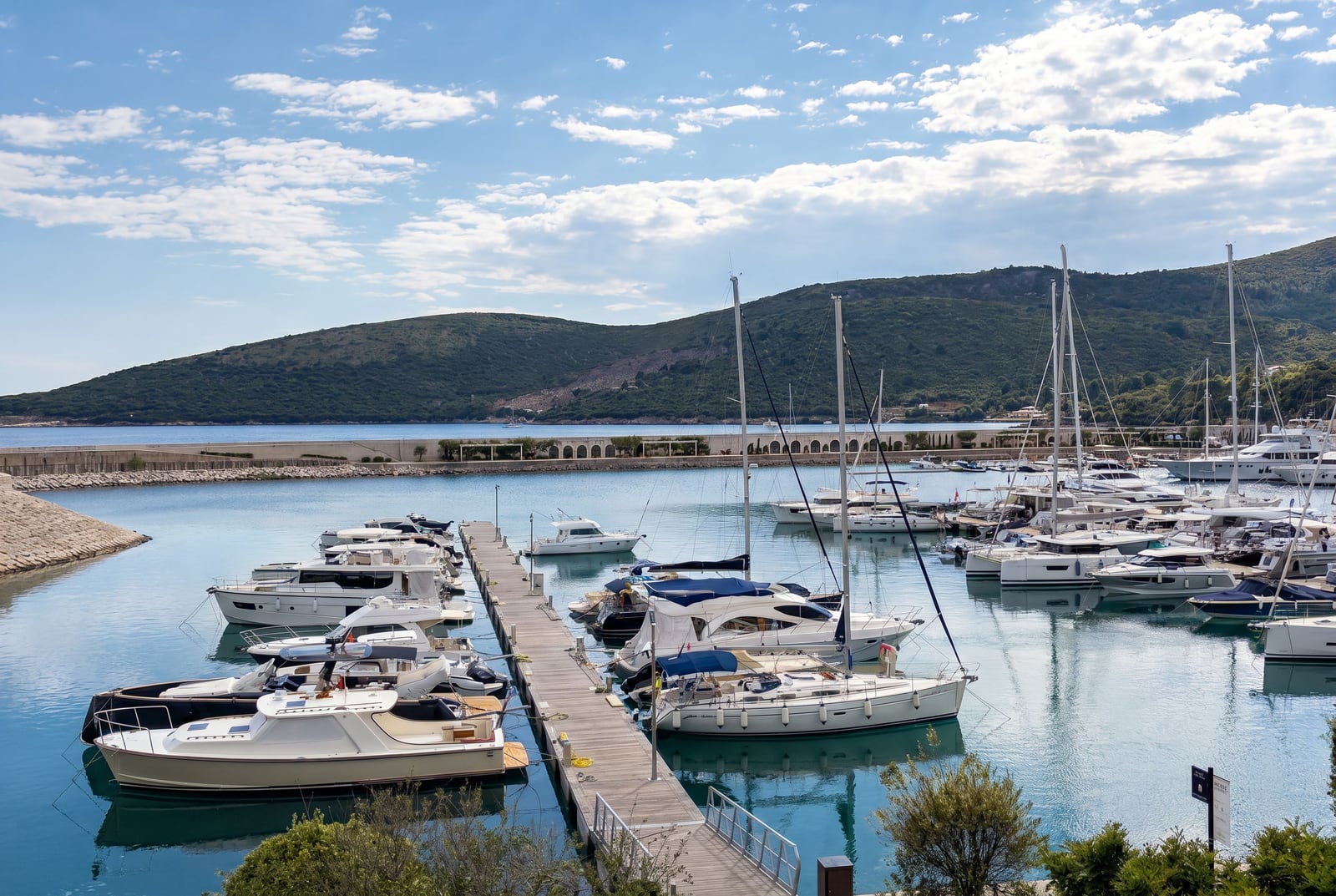 View of the yacht marina in Luštica Bay, Montenegro: a pier with snow-white yachts against the backdrop of mountains and the Adriatic Sea.