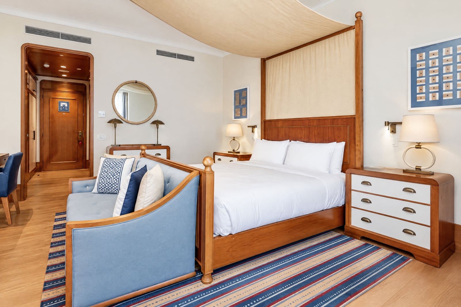 Bedroom featuring a wooden bed, blue sofa, striped rug, round mirror, and nightstands with lamps.