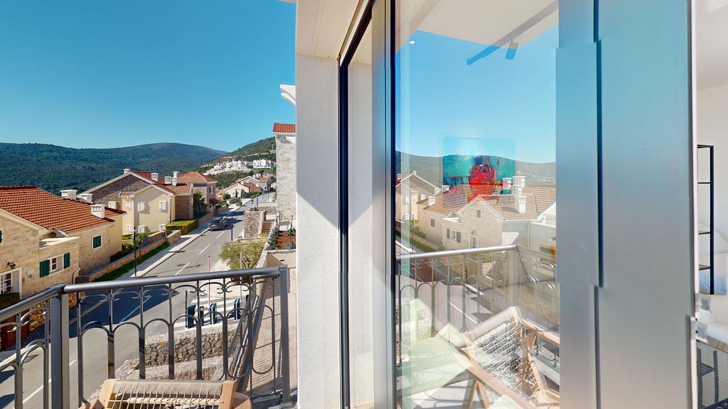 View from the balcony of a modern apartment in Luštica, Montenegro: panoramic windows, wrought iron railing, and mountain landscape.