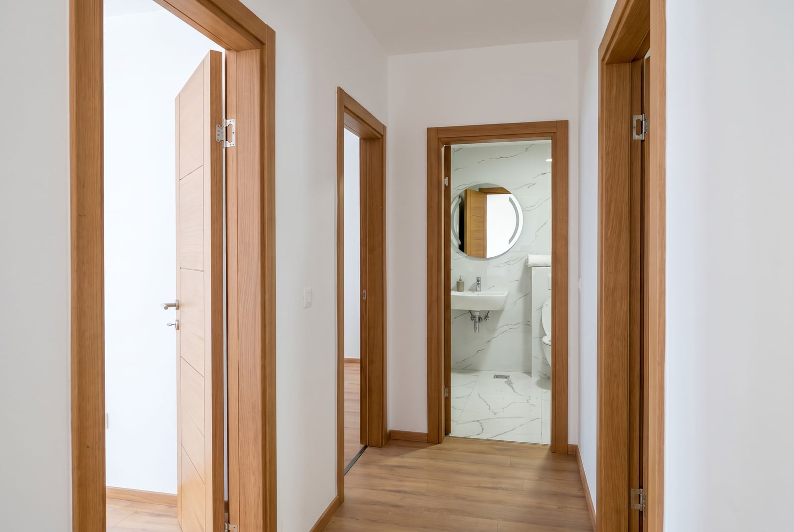 Bright hallway in an apartment in Pržno, Montenegro: wooden doors, laminate flooring, and entrance to a bathroom with marble-style finishes.