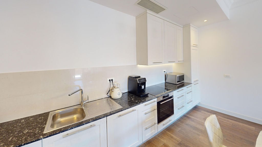Modern white kitchen with a dark countertop in an apartment at Luštica Bay, Montenegro: built-in appliances and a bright interior.