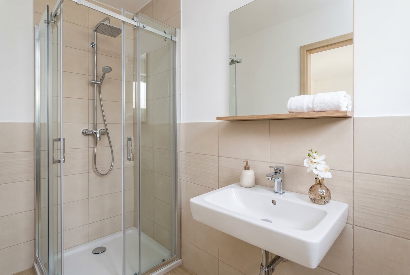 Modern bathroom with a walk-in shower in a Budva apartment, Montenegro: beige tiles, sink, and mirror.