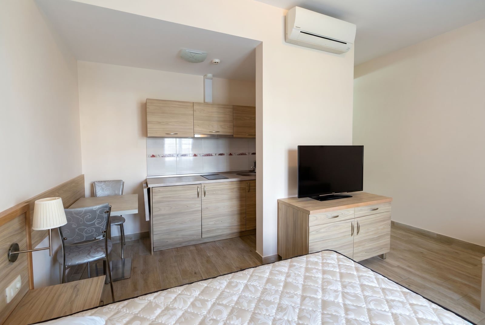 Interior of a living room with a kitchen in an apartment in Bečići, Montenegro: light-colored furniture, dining area, and TV stand.