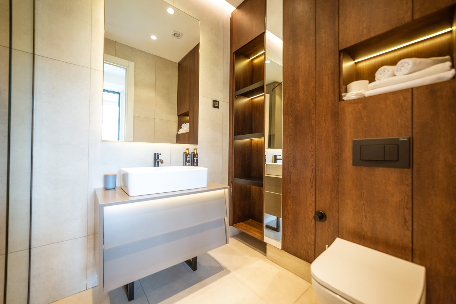Modern bathroom in an apartment in Bečići, Montenegro: stylish wooden furniture, lighting, and plumbing fixtures.