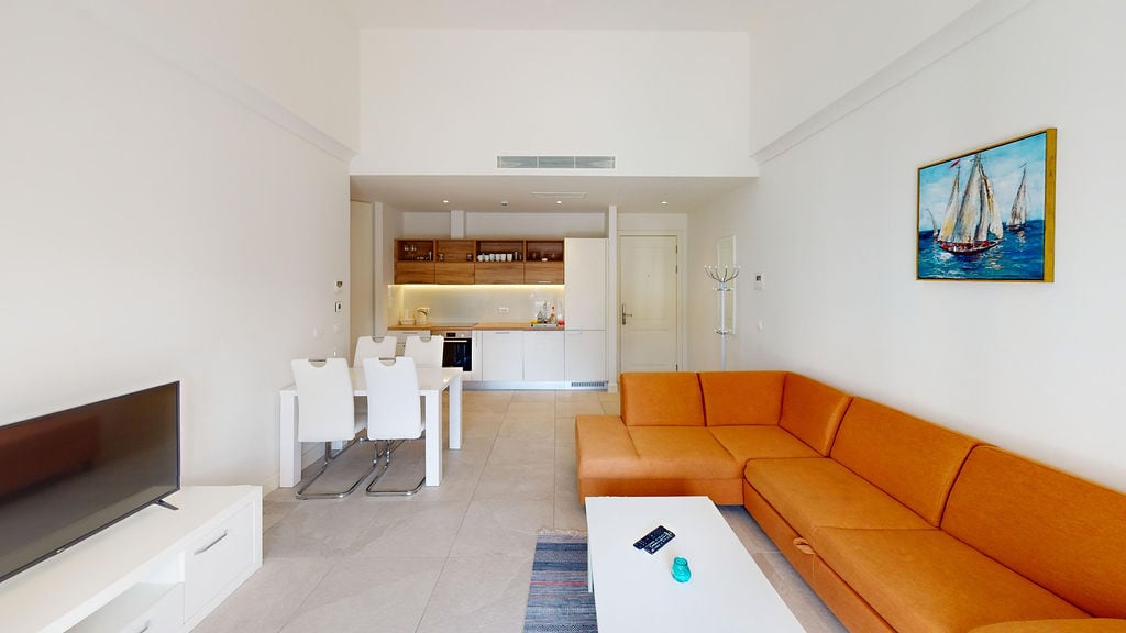 Modern living room with an orange sofa and kitchen in an apartment, Luštica, Montenegro. Bright interior with a dining area.