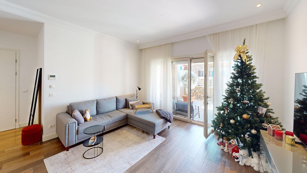 Bright living room with a gray sofa and a Christmas tree in an apartment, Luštica Bay, Montenegro. Access to the terrace, modern interior.
