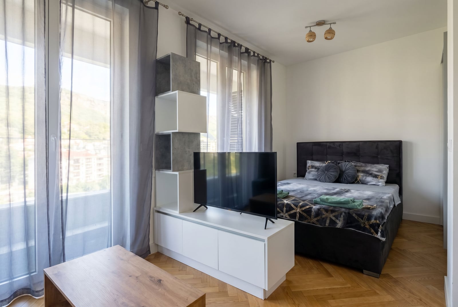 Modern bedroom with a double bed and TV area in a Becici apartment, Montenegro, featuring mountain views.