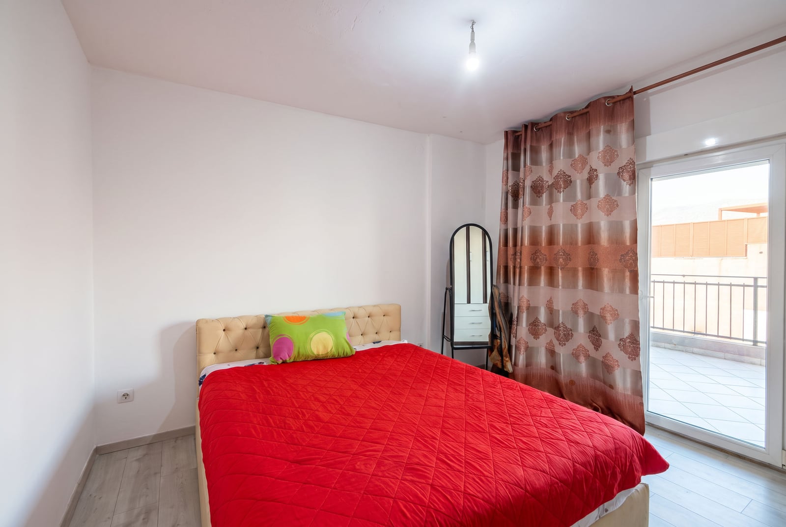Bright bedroom with a double bed, red bedspread, and access to a balcony in an apartment in Budva, Montenegro.