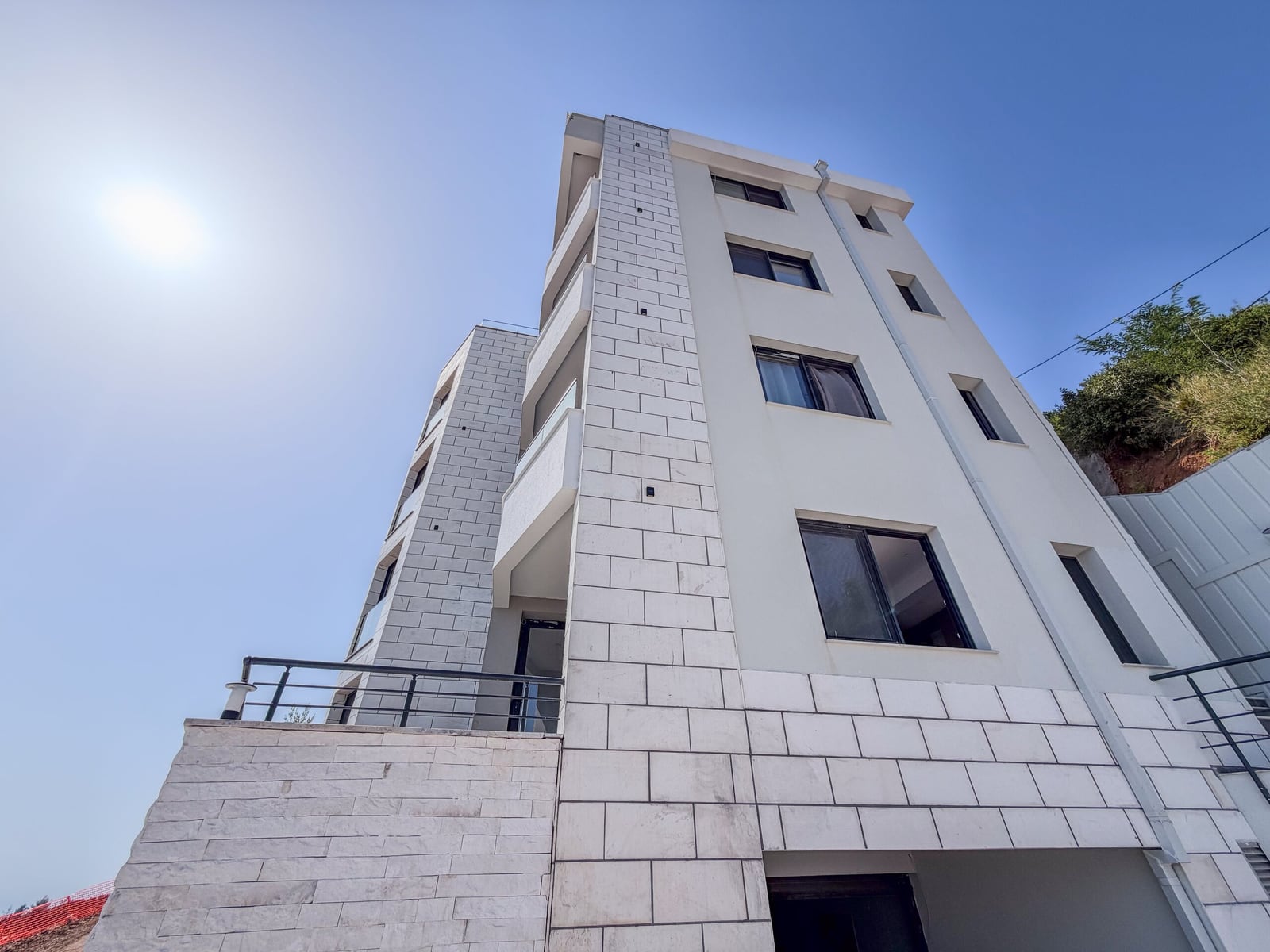 Low angle view of a multi-story white building with stone cladding and balconies against the sky.