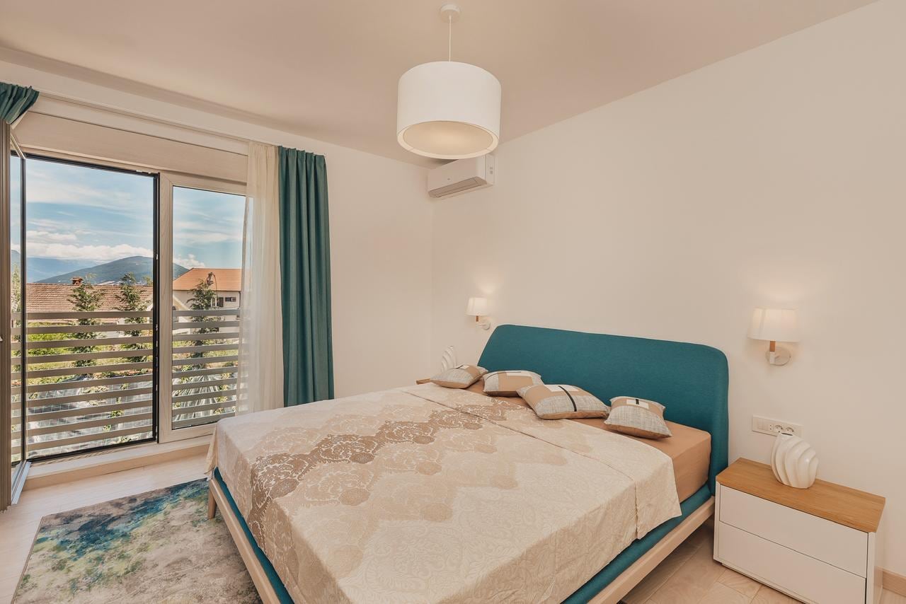Bright bedroom with a double bed and balcony access featuring mountain views in an apartment, Igalo, Montenegro.