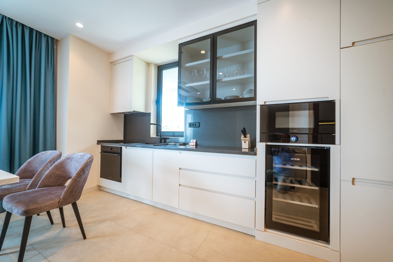 Modern kitchen in an apartment in Bečići, Montenegro: white facades, built-in appliances, wine cooler, and dining area.