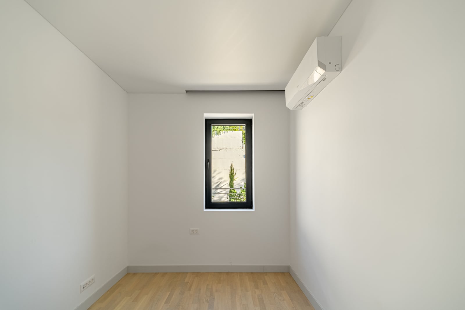Bright bedroom with parquet flooring and air conditioning in a townhouse, Kavac, Montenegro. Minimalist interior with a window.
