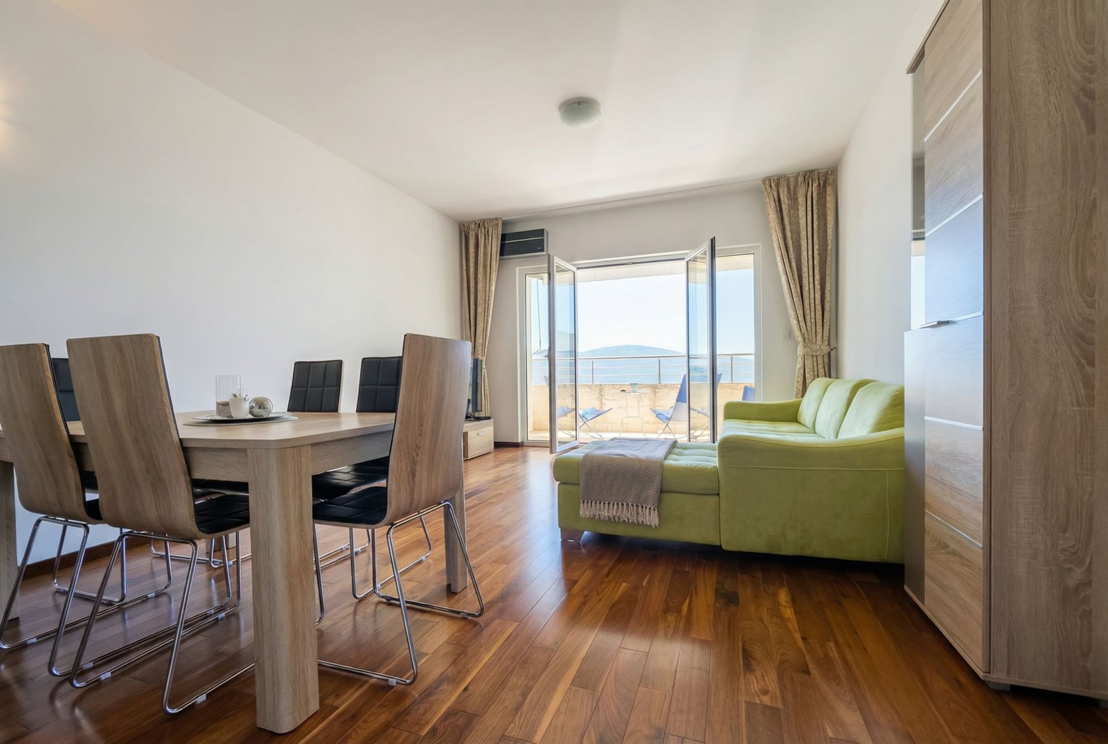 Living room in an apartment in Tivat, Montenegro: a bright room with a dining area, a green sofa, and access to the terrace.