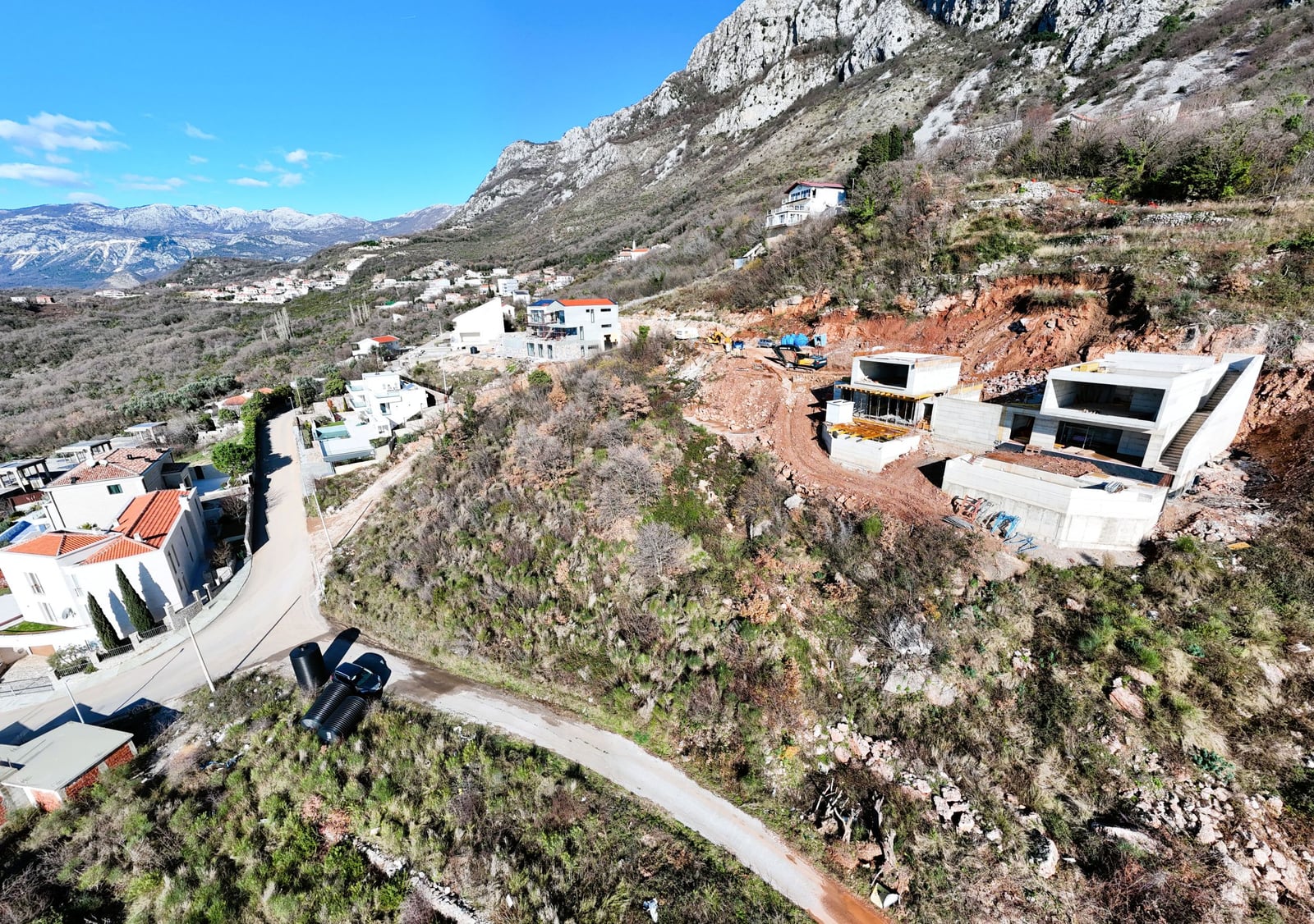 Villas under construction on a land plot in Blizikuće, Montenegro: aerial view of the mountain landscape and infrastructure.