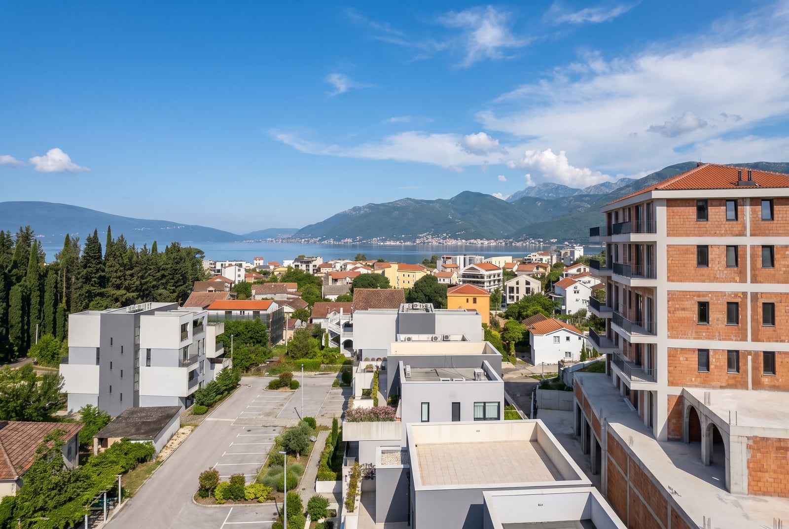 Aerial view of a coastal town with houses, parking lot, sea, and mountains.