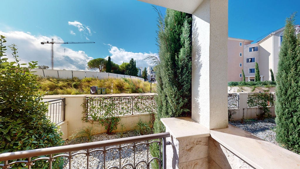 View from the balcony of an apartment in Luštica, Montenegro: a stone-finished terrace, decorative cypress trees, and landscaped design.