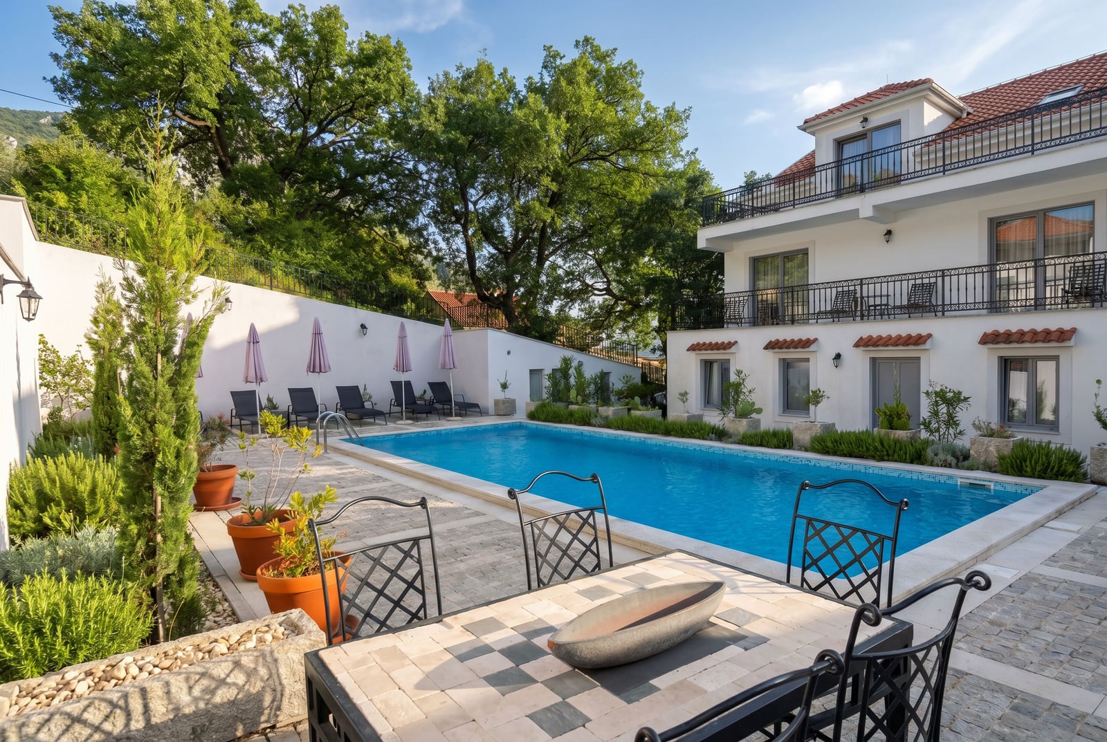 Pool and relaxation area at a villa in Risan, Montenegro: terrace with wrought iron furniture, sun loungers, and landscape design.