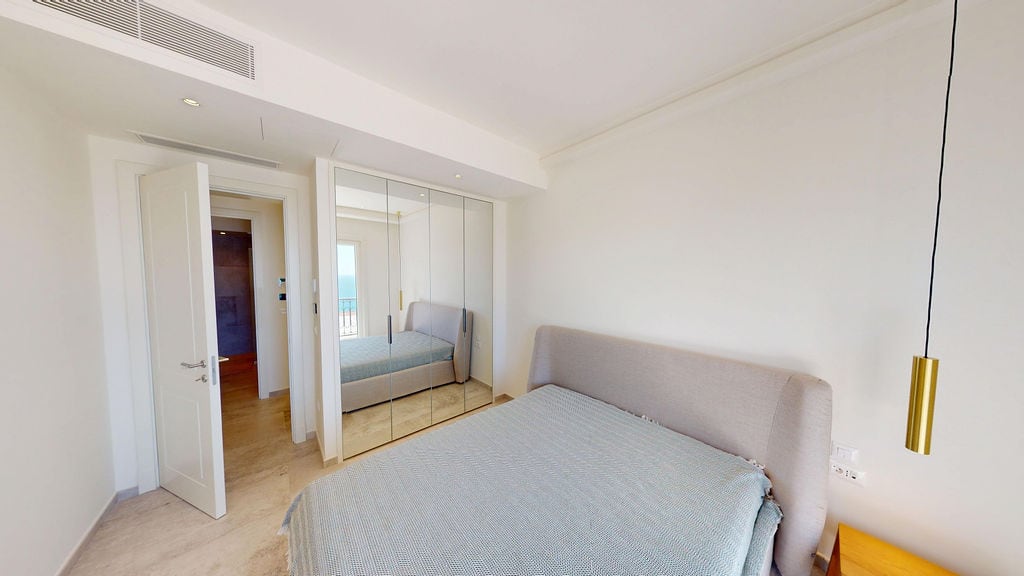 Modern bedroom with a double bed and mirrored wardrobe in the Luštica residential complex, Montenegro. Sea view from the window.