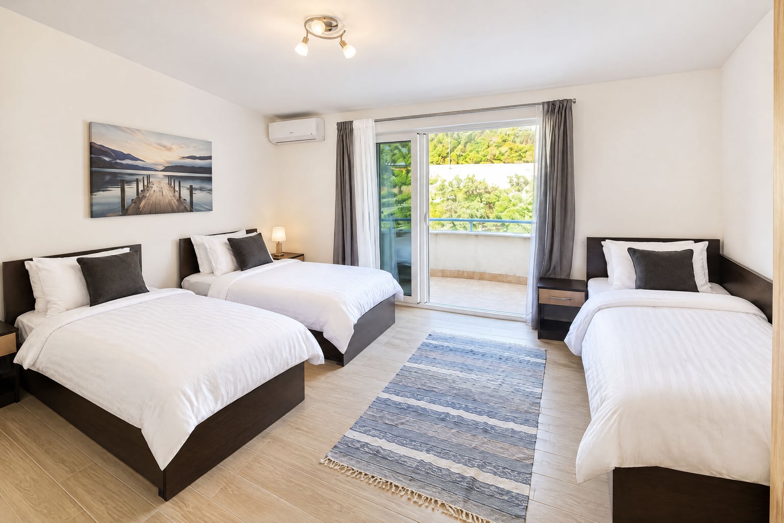Bedroom with three single beds, white bedding, a striped rug, and a sliding door leading to a balcony.