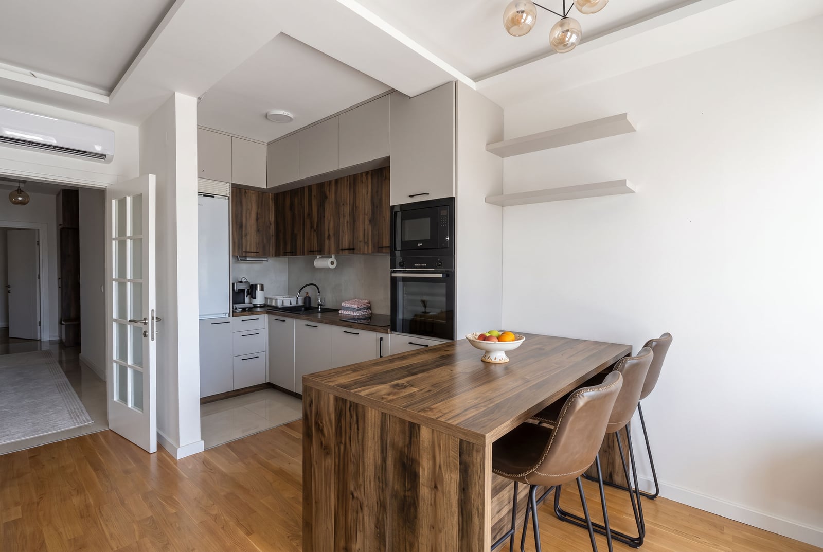 Modern kitchen featuring a wooden island, grey and wood cabinets, built-in appliances, and bar stools.