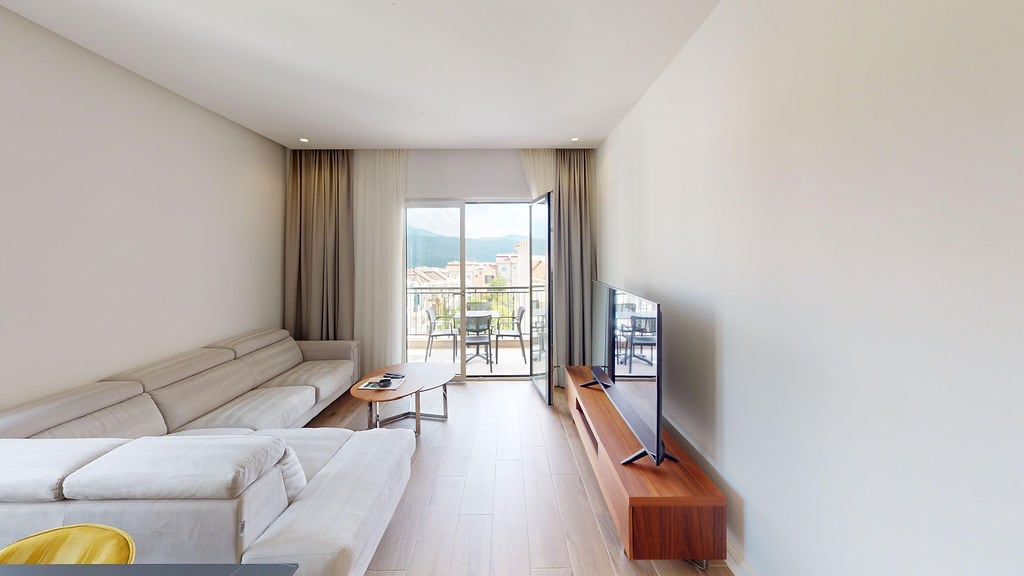 Bright living room in Luštica Bay apartments, Montenegro: modern furniture, TV area, and balcony access with a view.