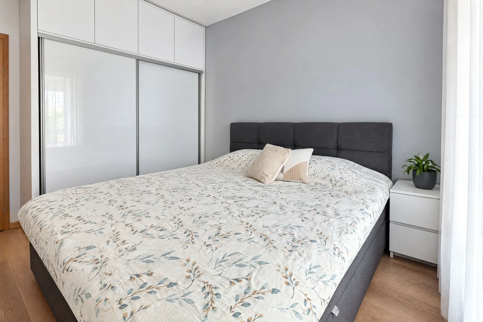 Modern bedroom featuring a double bed with floral bedding, white sliding wardrobe, and grey wall.